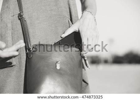 Closeup photo of stylish female taking cellphone out of handbag, sunny outdoors background. Black and white image