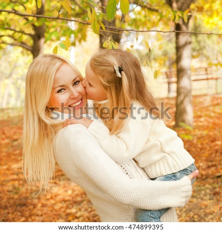 Little girl kissing her mother, smiling mother holding little baby girl, autumn outdoor