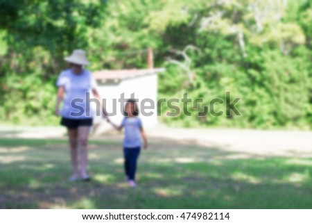 blurred picture of grandmother and granddaughter walking and holding hands in green garden, filtered color tone