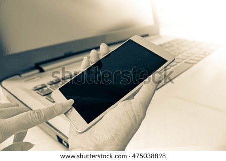 hand use smart phone on blur background of Laptop in sepia filter