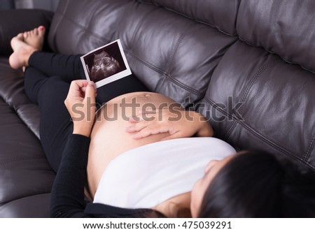 Pregnant woman resting on sofa and holding her child ultrasound picture