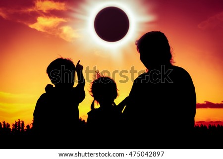 Silhouette back view of family sitting and relaxing together. Boy point to solar eclipse on gold sky background. Happy family spending time together. Outdoor. Royalty-Free Stock Photo #475042897