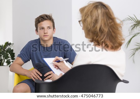 Mature psychologist doing notes, talking with a young patient, light interior Royalty-Free Stock Photo #475046773