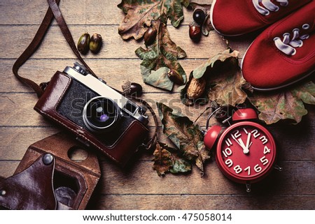 photo of the beautiful camera, gumshoes, clock and fallen leaves on the brown wooden background