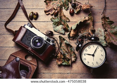 photo of the beautiful camera, fallen leaves and alarm clock on the brown wooden background