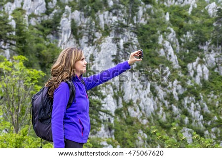 Young happy woman having fun outdoors, taking photos while standing on the top of the cliff