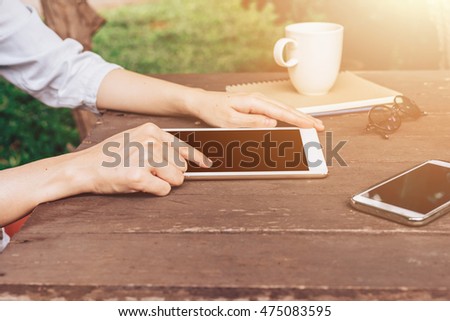 Hand woman using tablet on table in garden at coffee shop with vintage toned.
