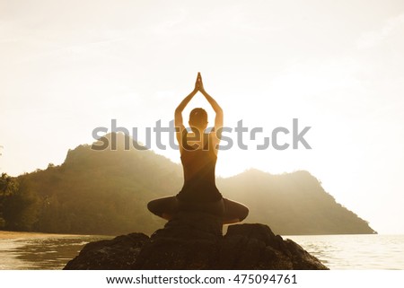 Young fit woman using yoga technique for meditation and wellbeing on beach at sunrise, Lens Flare