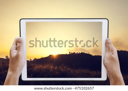 Hand holding digital tablet take a photo of sunset on the mountain in summer