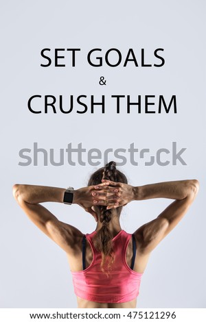 Back view of beautiful young person wearing red sportswear bra on grey background. Athletic model girl wearing smartwatch posing with hands behind head. Motivational phrase "Set goals and crush them"
