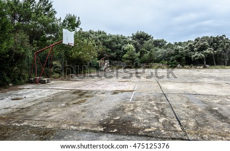 Old abandoned school sports court or schoolyard for different activities. Ruins of a sport venue abandoned long time ago with soccer, handball or football goals, basketball hoops and boards 