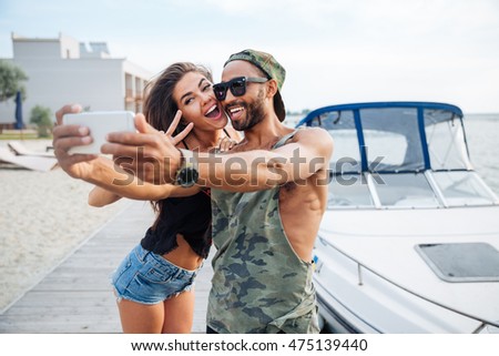 Portrait of a happy couple making selfie photo on smartphone outdoors at the sea pier