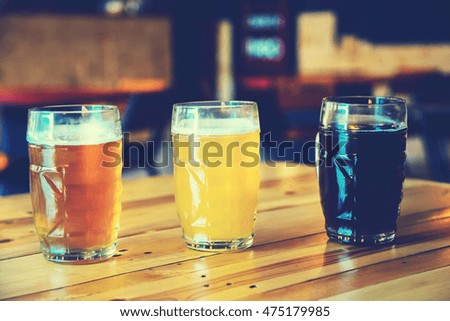 Beautiful background of the Oktoberfest. Glasses of cold fresh white, light and dark beer on the wooden bar counter in the pub. Assorted alcohol in a Flight Ready for Tasting. Blue toned