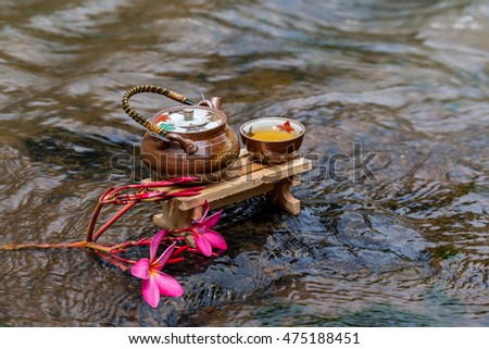 Cup of tea placed on a wooden table in a small stream of water from a waterfall
