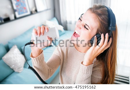 Funny portrait young woman with headphones singing and listening to music at home