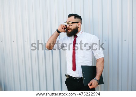 businessman stands with documents in hand and talking on the phone against a white wall