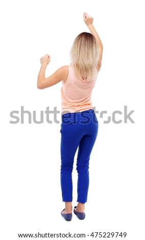 back view of dancing young beautiful woman. girl watching. Isolated over white background. Blonde in blue pants waving dancing raising his hands.