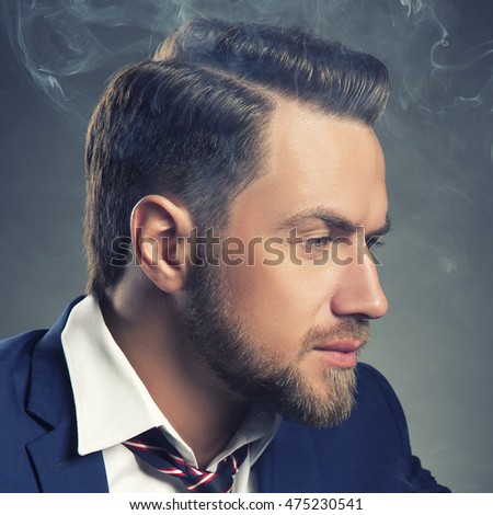 Young handsome bearded caucasian man. Perfect skin and hairstyle. Wearing suit. Studio portrait on gradient black to grey background. Toned