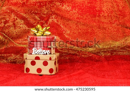 Christmas background with stacked holiday presents with gold bow and Believe text on royal red sparkle fabric 