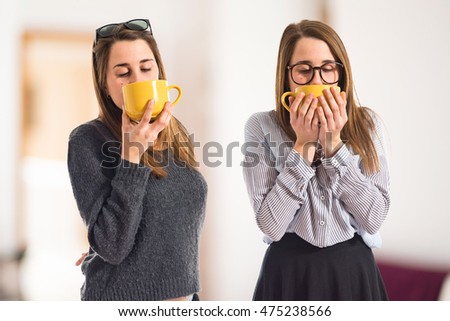 Twin sisters holding a cup of coffee on unfocused background