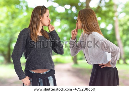 Twin sisters making silence gesture on unfocused background