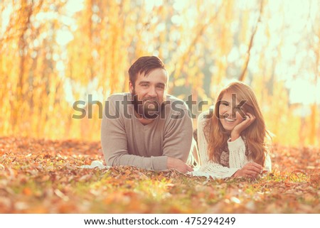 Couple in love lying on fallen autumn leaves under a tree in a park, enjoying a wonderful autumn day in nature
