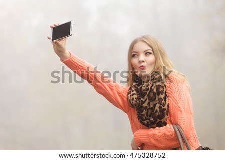 Lovely fashion woman in fall autumn park taking selfie self photo picture. Pretty cute young girl in sweater pullover with handbag photographing.