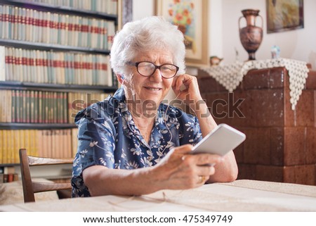 Portrait of a happy senior woman listening to music on smartphone at home. Royalty-Free Stock Photo #475349749