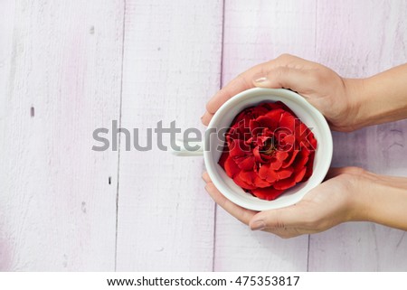 Top view on female hands holding cup with rose flower, wooden table background