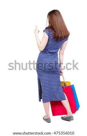 back view of woman with shopping bags pointing . brunette in a blue striped dress standing with shopping bags showing thumbs up.