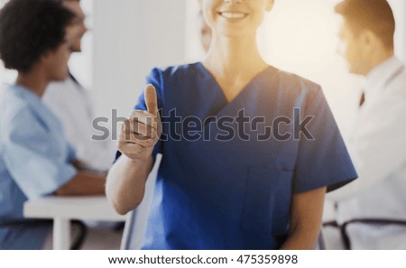 hospital, gesture, health care, people and medicine concept - close up of doctor or nurse showing thumbs up over group of medics meeting at hospital