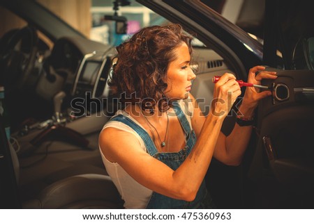 beautiful mechanic woman in a blue overalls repair the car door with a screwdriver. instagram image filter retro style