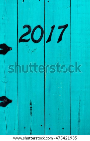 Year 2017 in black iron numbers hanging on antique rustic teal blue wooden door; Happy New Year background