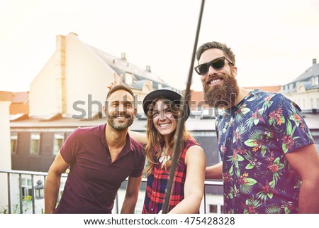 Woman and two male friends stand on patio and smile towards the camera as she makes bunny ears on one of them