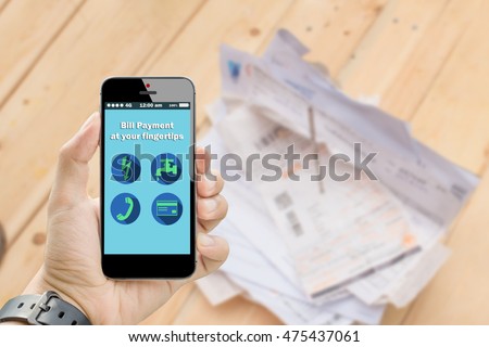 hand holding smart phone online bill payment at your fingertips with utilities bill on wooden table in background Royalty-Free Stock Photo #475437061