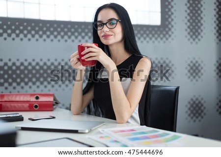 Young successful business woman sitting at office table and confidently looking at the camera