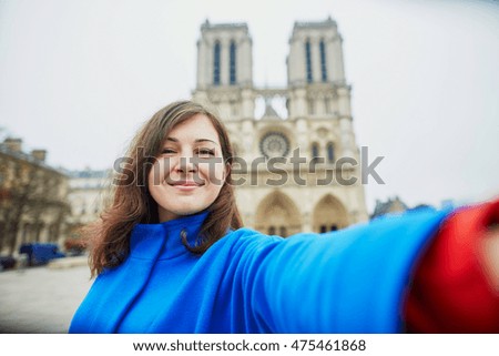 Beautiful young tourist in Paris, making funny selfie near Notre-Dame cathedral