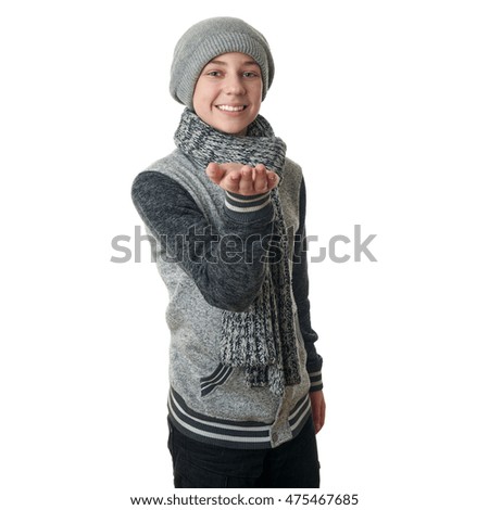 Cute teenager boy in gray sweater, hat and scarf holding something over white isolated background, half body
