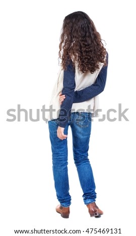 back view of standing young beautiful woman. Long-haired girl with curly hair standing with his hands behind his back.