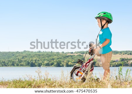 Child riding a bicycle. Child with a bicycle on the river bank. Kid in a helmet riding a bike in the forest. Toned image.