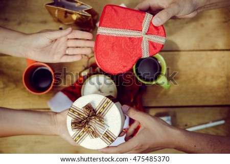 Top view picture of male and female hand above table with gift boxes and Santa Claus hat. Closeup of holiday planning with alarm clock and coffee cup on wooden plank background.