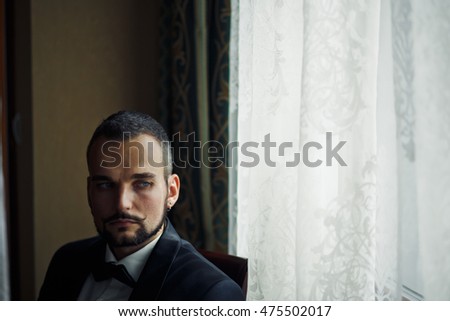 The handsome groom  sits near window in room