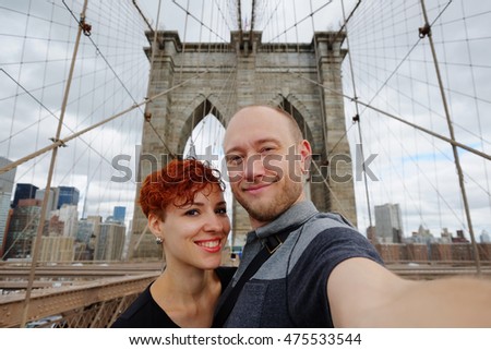 Happy selfie tourist woman and man taking self-portrait picture with smart phone on Brooklyn Bridge, New York City, Manhattan, USA. Young beautiful family couple travel, photographing NY landmarks.
