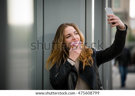 Young woman taking selfie with mobile phone while eating donut in street