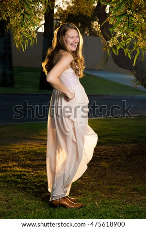 A beautiful, blond, teenage girl twirls her skirt in the sunlight.  She is backlit and laughing with an open mouth.
