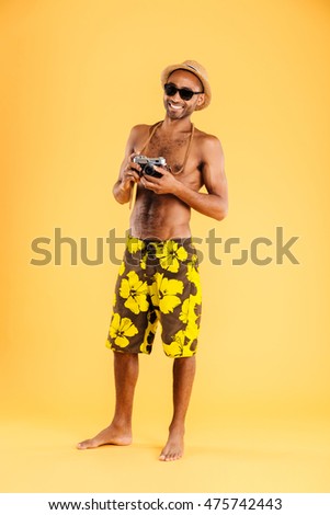 Full length portrait of a happy afro american man holding retro photo camera isolated on a orange background