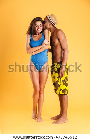 Loving young couple in swimwear kissing isolated on the orange background