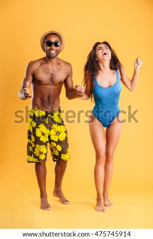 Young beautiful happy cheerful couple in beachwear holding hands isolated on the orange background