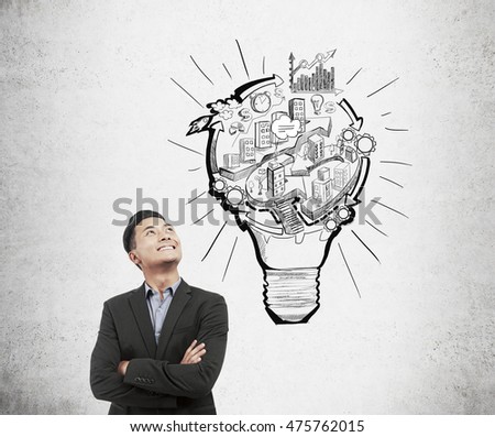 Asian businessman standing near concrete wall with light bulb and city sketches. Concept of city planning