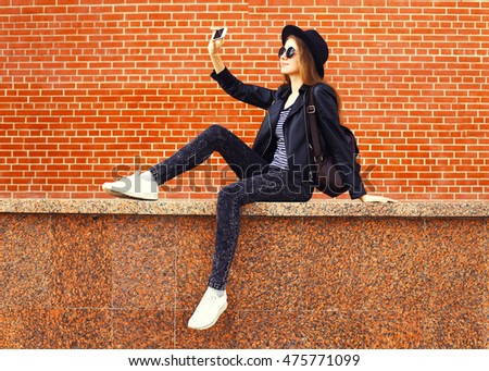 Fashion young woman taking selfie with smartphone in rock black style on city street background